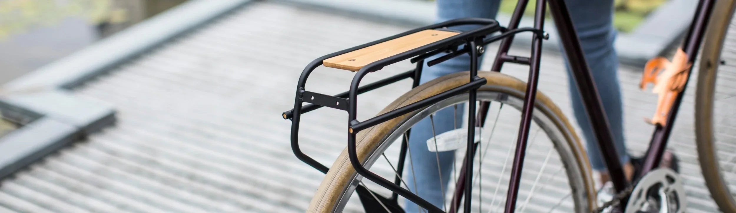 Everyday cargo rack with bamboo deck on the back of a purple single speed bicycle being walked by a rider in jeans