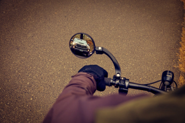 Watch Your Back XL bicycle mirror on a handlebar with a rider's hand underneath.