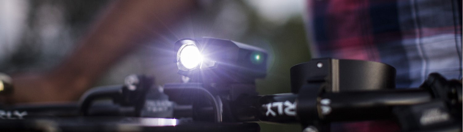 A PDW front bike light, lit up and mounted to a bike handlebar.