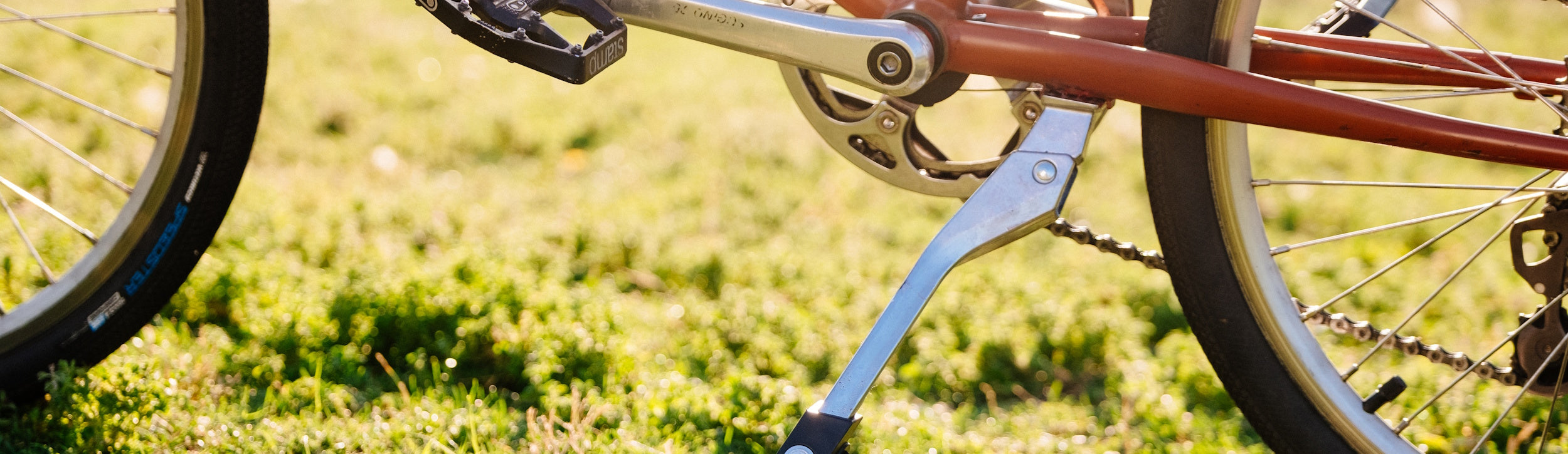 A Sturdy Lad kickstand on an orange bike on green grass with sunshine in the background