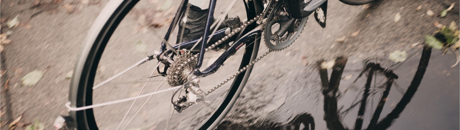 A rear wheel of a road bike with PDW fenders, being ridden through a puddle.