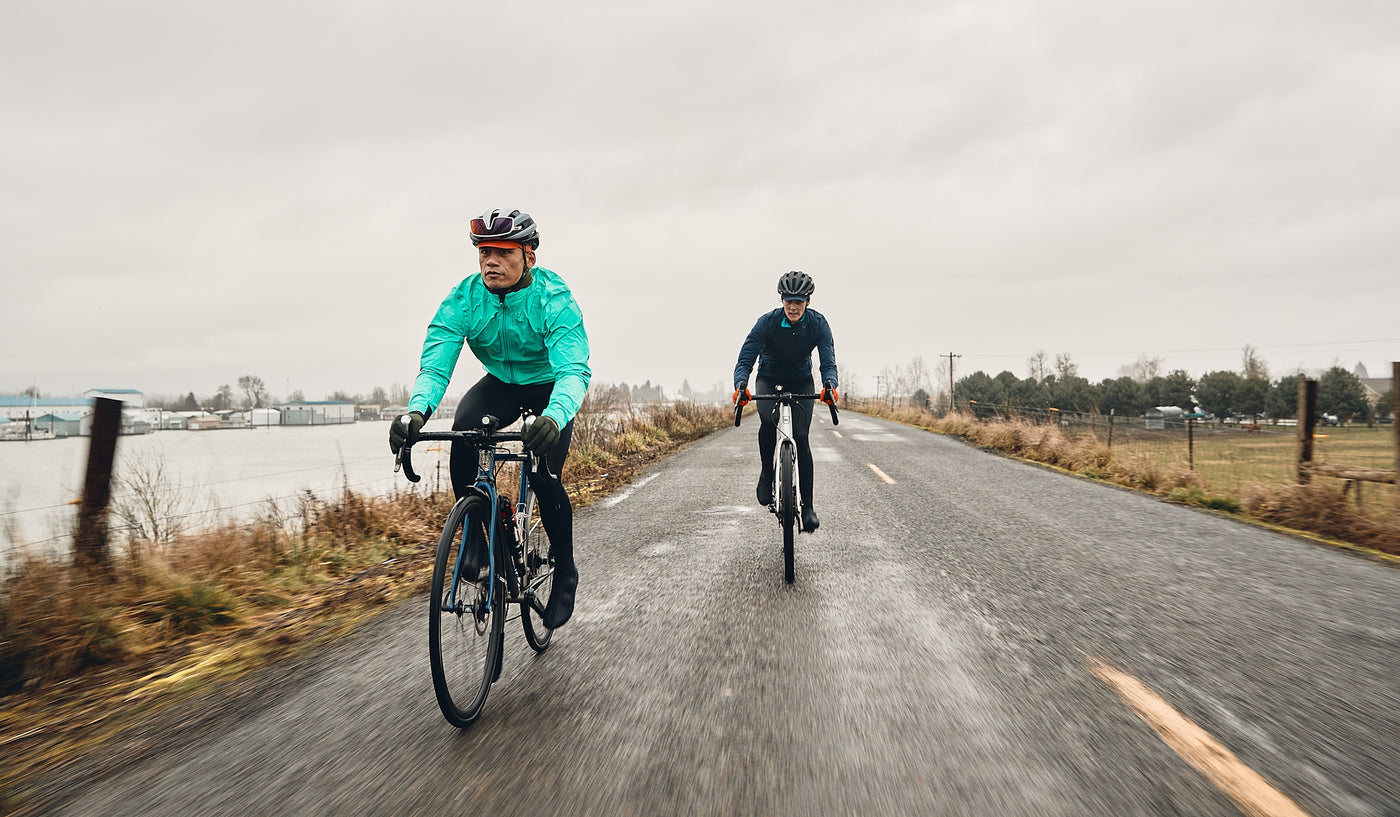 Two cyclists riding in the rain with fenders and lights